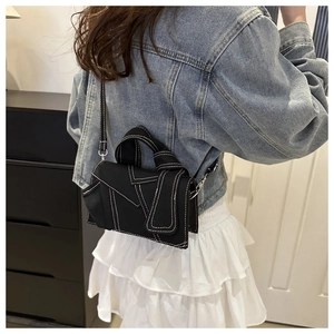 Detail of a black canvas crossbody bag featuring white contrast stitching and a knotted handle