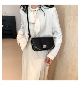 Close-up of black leather crossbody bag with silver buckle and delicate chain strap