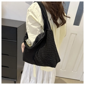 Detailed view of a black pleated tote bag worn by a model in a minimalist setting