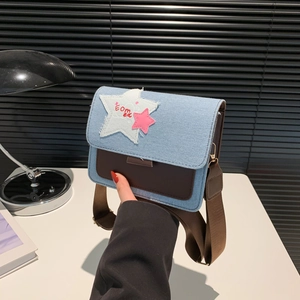 Denim and leather crossbody bag with star patch and wide strap held in hand
