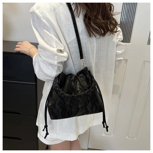 Detail of black pleated bucket bag with braided handle and adjustable shoulder strap