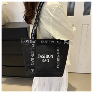 Detail of black canvas tote bag with white FASHION BAG lettering worn by a model