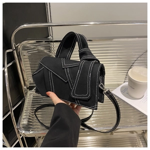 Detailed close-up of a black denim patchwork handbag with white contrast stitching and silver buckle