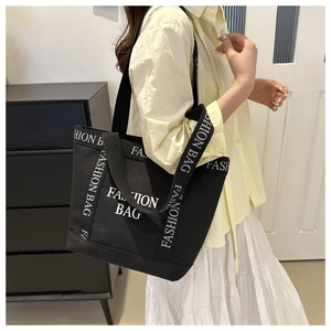 Detail of black canvas tote bag with white Fashion Bag lettering and woven shoulder strap