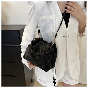 Detail of black drawstring bucket bag with woven handle and gold chain strap