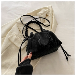 Detail of black pleated faux leather bucket bag with woven handle and drawstring accents