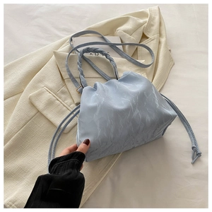 Detail of light blue cloud bag with marble texture and woven handle on beige suit