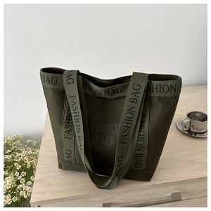 Detail of dark green canvas tote bag showing fashion letter straps on a wooden table