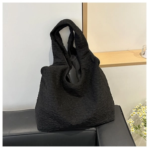 Close-up of black seersucker pleated tote bag with wrinkled texture on a leather sofa