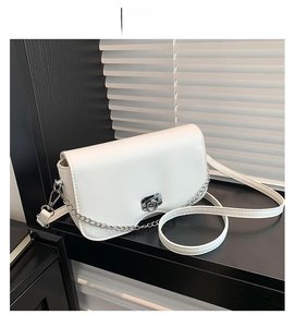 White crossbody bag with wavy bottom design and silver ring lock on black surface
