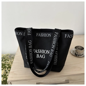 Detail of black canvas tote bag showing white Fashion Bag letters and wide shoulder strap