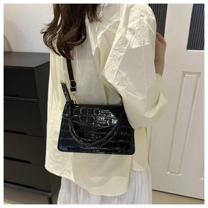 Detail of black stone-pattern leather crossbody bag with golden metal buckle on model