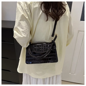 Black crocodile pattern crossbody bag with twin handles and adjustable strap on a model