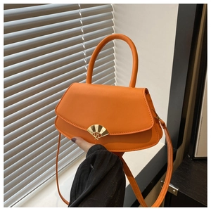 Détail du sac à main orange en cuir avec fermoir éventail doré et logo sur un rebord de fenêtre