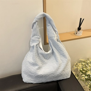 Minimalist light blue pleated shoulder bag with textured fabric on a black sofa