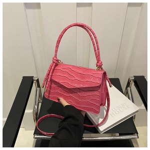 Close-up of rose pink crocodile pattern crossbody bag with knot fringe on a leather chair