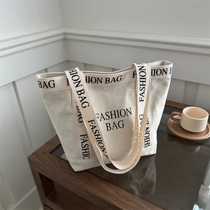 Large cream canvas tote bag with black letter print on a stylish wooden side table