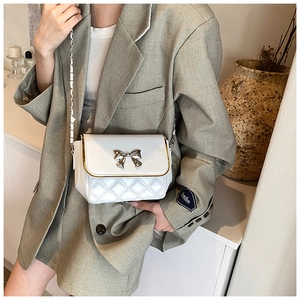 Detail of white quilted crossbody bag with a golden bow clasp and chain strap