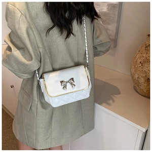 Detail of white quilted crossbody bag with silver bow clasp and elegant chain strap