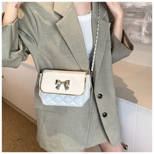 Close-up of white quilted crossbody bag featuring a golden metal trim and bow clasp
