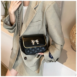 Detail of black quilted crossbody bag featuring a silver bow and metal chain strap