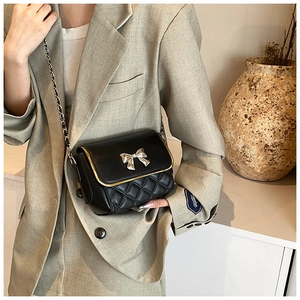 Detail of black quilted crossbody bag with silver bow and gold piping on the flap