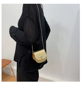 Detail showing gold crocodile pattern mini saddle bag with chain on a black knit sweater