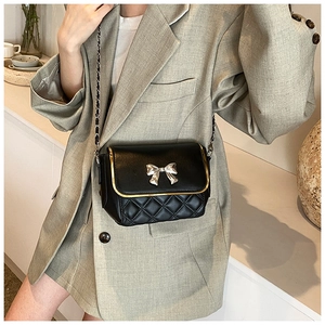 Quilted black chain crossbody bag with silver bow detail worn with a casual khaki blazer
