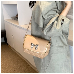 Close-up of beige quilted crossbody bag with silver bow detail and metal chain strap