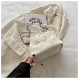 Detail of cream bucket bag with translucent bead handle and silver chain on tweed jacket