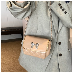 Detail of beige quilted crossbody bag with silver bow accent and metal chain strap