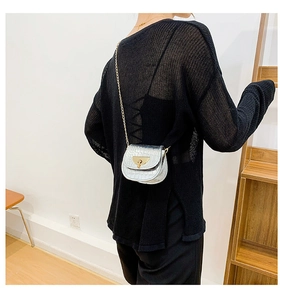 Detail of silver crocodile-embossed mini saddle bag with golden chain and lock on model