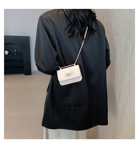 Detail of a white quilted mini crossbody bag with gold chain strap on a black blazer