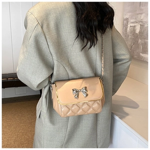 Detail of apricot quilted crossbody bag with silver bow clasp and metal chain strap