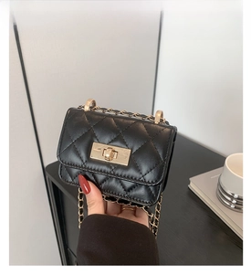 Detail of mini black quilted bag with gold chain strap and metal clasp held in hand