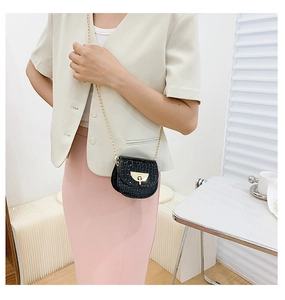 Detail of black crocodile texture saddle bag with gold metal buckle and chain strap