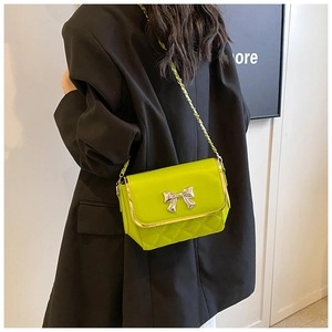 Detail of neon green quilted bag with silver bow ornament and metallic chain strap