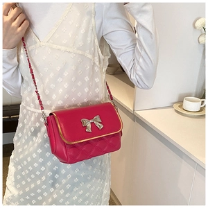 Detail of rose red quilted crossbody bag with silver bow and metal chain strap