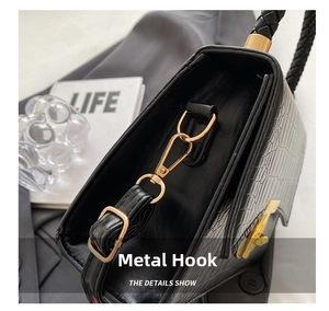 Detail view of gold hardware hook and woven handle on black crocodile pattern handbag