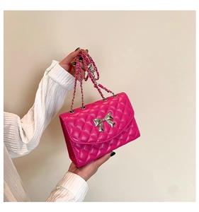 Détail d'un sac matelassé magenta avec nœud argenté et bandoulière en chaîne
