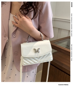 Detailed side view of white quilted crossbody bag with silver butterfly buckle