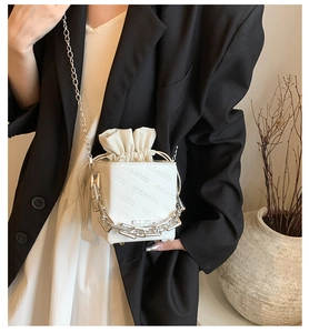 Detail of white leather crossbody bag showing embossed rich rabbit letters and metal chains