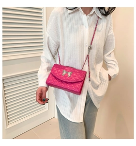 Sac bandoulière fuchsia matelassé avec nœud argenté porté sur une chemise blanche