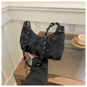 Détail du sac plissé noir en demi-lune avec poignée tressée dans un décor de café