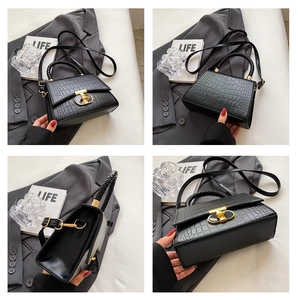 Detail view of black crocodile pattern handbag with woven handle and gold T-lock