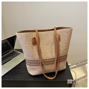 Detail of a woven tote bag with brown leather handles on a minimalist desk