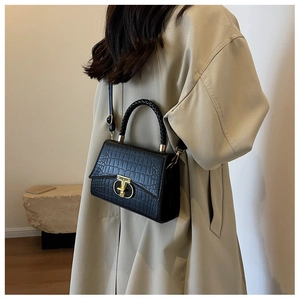 Detail of black crocodile texture handbag with gold T-lock and woven handle on model
