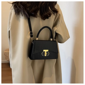 Close-up of black crocodile pattern handbag with woven handle and gold T-lock detail