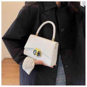 Detailed view of white croc-embossed handbag with gold clasp and woven rope handle