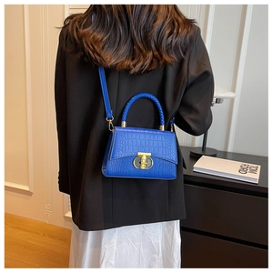 Detail of bright blue faux crocodile leather bag with braided handle and gold clasp